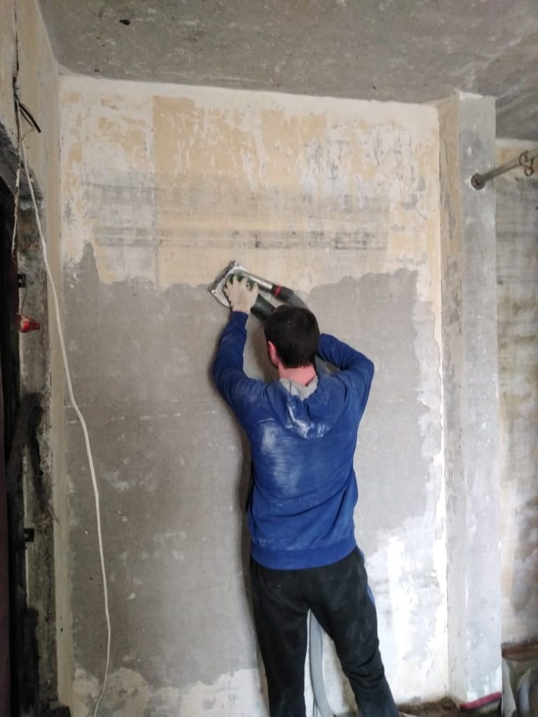 Зачистка стен от старой шпаклевки, мастер в процессе работы